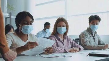 nel un' luminosa aula, diverso Università studenti indossare maschere mentre collaboratore su un' progetto. essi scambio Appunti e idee, sottolineando lavoro di squadra e formazione scolastica nel un' Università ambientazione. video