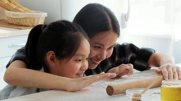 A mother and her daughter joyfully share a moment in the kitchen, rolling dough and preparing ingredients. Their laughter and affection highlight the warmth of family life at home. video