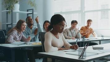 en grupp av olika högskola studenter är arbetssätt tillsammans i en ljus, rymlig klassrum. ett studerande fokuserar spänt på tar anteckningar medan andra mobbning henne video