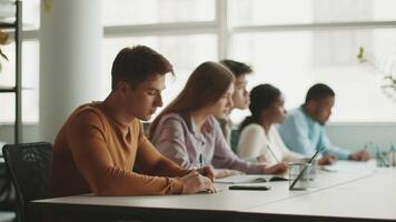 A diverse group of college students sits at a long table, concentrating on their studies. video