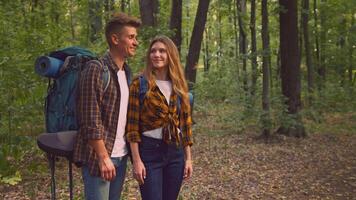 A couple stands together in a vibrant forest, smiling as they embrace the outdoors. They are dressed in casual hiking attire, ready for a day of adventure and exploration through nature's beauty. video