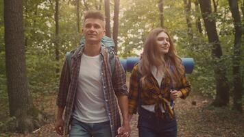 A couple enjoys a hike in a forest, exploring nature together with backpacks. The sun filters through the trees, creating a warm and inviting atmosphere as they walk hand in hand. video