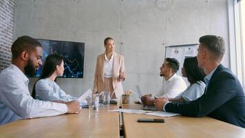 A team of multiethnic professionals engages in a business meeting, discussing strategies and analyzing graphs on a screen. The atmosphere is focused and collaborative, fostering ideas for growth. video