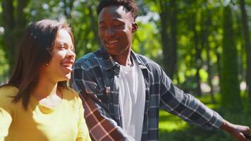 A young African American couple smiles as they cycle side by side through a lush green park, enjoying the warmth of the sun and each other's company on a beautiful day outdoors. video