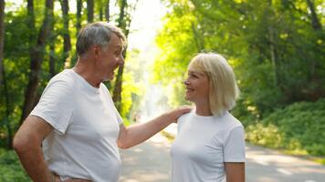A senior couple in their 60s jogs together in a beautiful park surrounded by lush greenery. They share smiles and laughter, embodying an active and healthy lifestyle. video
