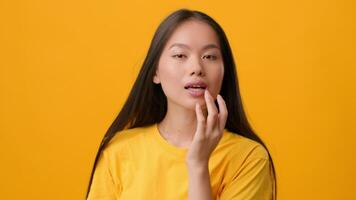 A young woman of Asian descent, dressed in a bright yellow shirt, poses confidently against a striking yellow backdrop. Her long hair flows gently as she engages playfully with the camera. video