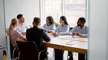 A group of diverse professionals engages in a strategic meeting at a contemporary office. They share ideas and insights while seated at a large table with documents and beverages present. video