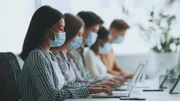 A group of diverse college students focuses on their laptops during a study session. They are seated in a modern classroom, engaged in collaborative learning amidst a backdrop of plants. video