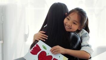 In a warm kitchen, a mother and her daughter embrace, showcasing their strong bond. The daughter proudly holds a colorful drawing while enjoying their quality time together. video