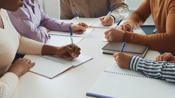 In a collaborative environment, several diverse students gather around a table, taking notes in notepads while discussing academic concepts. Their focus reflects dedication to learning. video