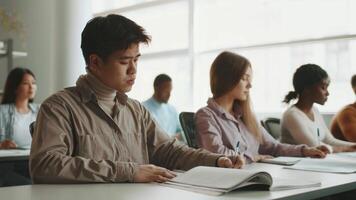 In a university classroom filled with natural light, diverse students focus intently on their studies. Each person participates quietly, writing notes and preparing for academic success. video