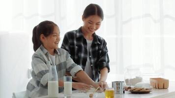 In a bright kitchen, a mother and daughter bond while preparing food together. They smile and share laughter as they roll out dough, creating a warm atmosphere of love and togetherness. video