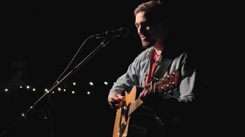 A musician is playing guitar on a large stage with audience members holding flashlights in the background. The auditorium is filled with beautiful flashing lights. 17 video