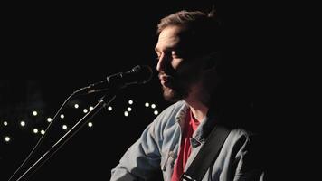 A musician is playing guitar on a large stage with audience members holding flashlights in the background. The auditorium is filled with beautiful flashing lights. 5 video