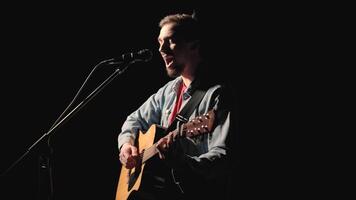 A musician is playing guitar on a large stage with audience members holding flashlights in the background. The auditorium is filled with beautiful flashing lights. 39 video