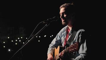 A musician is playing guitar on a large stage with audience members holding flashlights in the background. The auditorium is filled with beautiful flashing lights. 4 video
