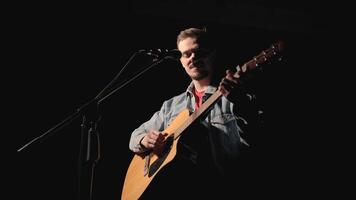 A musician is playing guitar on a large stage with audience members holding flashlights in the background. The auditorium is filled with beautiful flashing lights. 43 video
