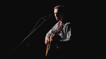 A musician is playing guitar on a large stage with audience members holding flashlights in the background. The auditorium is filled with beautiful flashing lights. 3 video