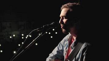 A musician is playing guitar on a large stage with audience members holding flashlights in the background. The auditorium is filled with beautiful flashing lights. 6 video