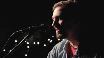 A musician is playing guitar on a large stage with audience members holding flashlights in the background. The auditorium is filled with beautiful flashing lights. 28 video