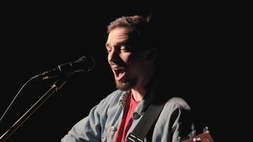 A musician is playing guitar on a large stage with audience members holding flashlights in the background. The auditorium is filled with beautiful flashing lights. 12 video