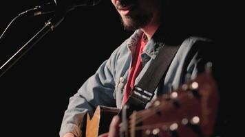 A musician is playing guitar on a large stage with audience members holding flashlights in the background. The auditorium is filled with beautiful flashing lights. 2 video