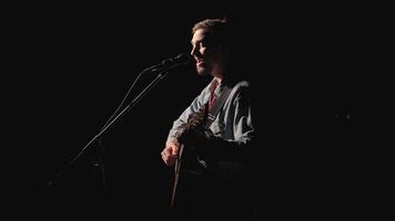 A musician is playing guitar on a large stage with audience members holding flashlights in the background. The auditorium is filled with beautiful flashing lights. video
