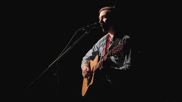 A musician is playing guitar on a large stage with audience members holding flashlights in the background. The auditorium is filled with beautiful flashing lights. 8 video