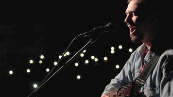 A musician is playing guitar on a large stage with audience members holding flashlights in the background. The auditorium is filled with beautiful flashing lights. 44 video