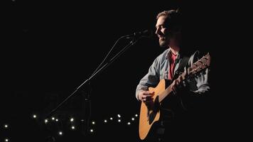 A musician is playing guitar on a large stage with audience members holding flashlights in the background. The auditorium is filled with beautiful flashing lights. 34 video