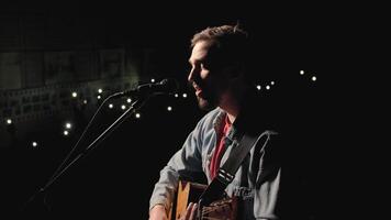 A musician is playing guitar on a large stage with audience members holding flashlights in the background. The auditorium is filled with beautiful flashing lights. 23 video