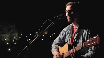 A musician is playing guitar on a large stage with audience members holding flashlights in the background. The auditorium is filled with beautiful flashing lights. 14 video