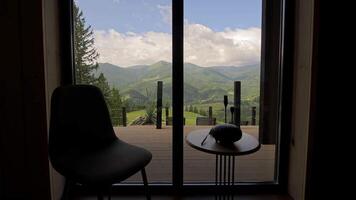 Mountain view from cozy cabin interior with deck. Peaceful view from inside a cabin looking out through glass doors to a wooden deck and green mountain video