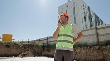 Construction worker using walkie-talkie at site. Male construction worker in safety gear communicating via walkie-talkie at a residential building site on a video