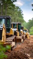 A line of yellow bulldozers parked on a dirt road photo