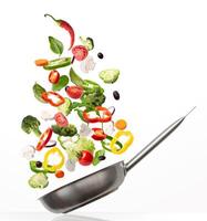 Preparing Healthy Meal. Creative collage of fresh vegetables flying into a pan, isolated on white background. Slices of tomato, lettuce, pepper and mushroom with broccoli, spinach and olives falling photo