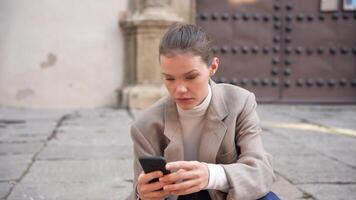 A professional woman is engaged with her smartphone while enjoying the outdoors in an urban setting video