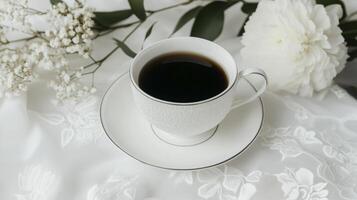 A cup of coffee and flowers on a white table photo