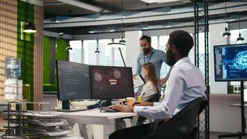 Programmer in office requesting help from coworkers to fix critical error warning. IT employee and colleagues brainstorming how to fix computer bug affecting systems, camera A video