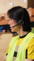 Vertical Call center male worker answer help line calls in a logistics warehouse, updating clients on orders and resolving cargo mix ups. Managing shipping software and airway bills. Camera B. video