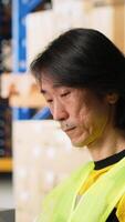 Vertical Worker verifying cardboard boxes and awb tags for parcel tracking, handling order processing before distribution. Man in hi vis vest working in e-commerce warehouse with industrial racks. Camera B. video