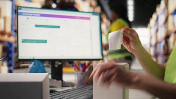 Asian employee applying shipping labels and scanning tracking info, registering the cargo information for parcel status during delivery. Manages labeling tasks with hi vis vest in depot. Camera A. video