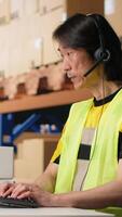 Vertical Call center employee assisting customers in a fulfillment center, handling inventory control and package tracking. Asian man resolving issues related to delivery delays or wrong addresses. Camera B. video