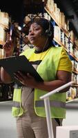 Vertical Black customer service worker speaks with clients about cargo issues, helping with the parcel information from the industrial warehouse. Woman resolves order mix up on headset. Camera A. video