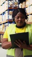 Vertical African American woman in hi vis vest handles calls on the help line, assisting people needing help with parcel tracking or other shipment information. E-commerce activity. Camera A. video