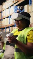Vertical Black female employee with virtual reality glasses handling orders fulfillment via 3D simulation, parcel status on package tracking software. Artificial intelligence inventory control. Camera A. video