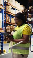 Vertical Black depot worker uses package tracking interface on tablet for inventory control for the delivery service, industrial warehouse filled with big storage racks. Online shopping logistics. Camera A. video