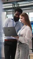 Vertical Junior dev and colleague in office reviewing AI system metrics, monitoring performance dashboards. Tech company programmer and young female engineer tuning neural networks, camera A video
