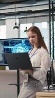 Vertical Portrait of young smiling female programmer in office automating repetitive tasks using AI scripts. Cheerful junior developer using artificial intelligence to speed up feature implementation, camera A video