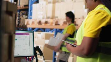 Warehouse employee using package tracking software on computer monitor, managing express delivery and using awb tracking info to update real time parcel status. Distribution hub. Camera B. video